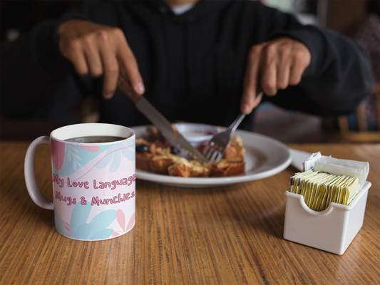 11oz funny coffee mug back side "My love language Mugs & Munchies" on table while person eats